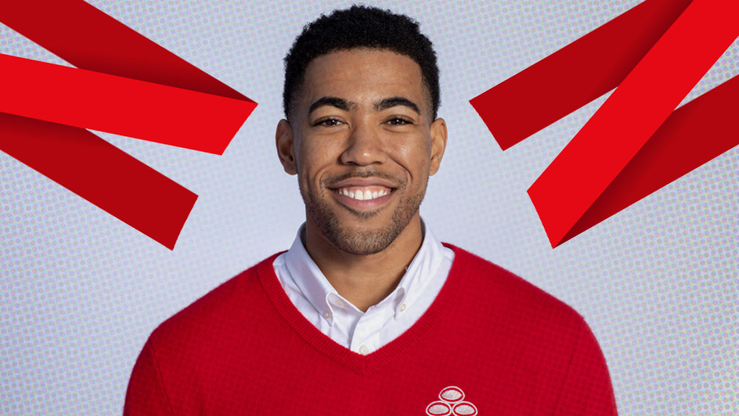 Friendly portrait: smiling man in a red sweater with a white shirt, decorative red ribbons overhead.